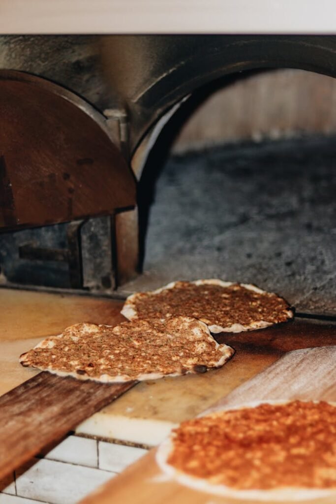 pexels-photo-16488564 Freshly baked flatbreads on wooden paddles by a stone pizza oven.